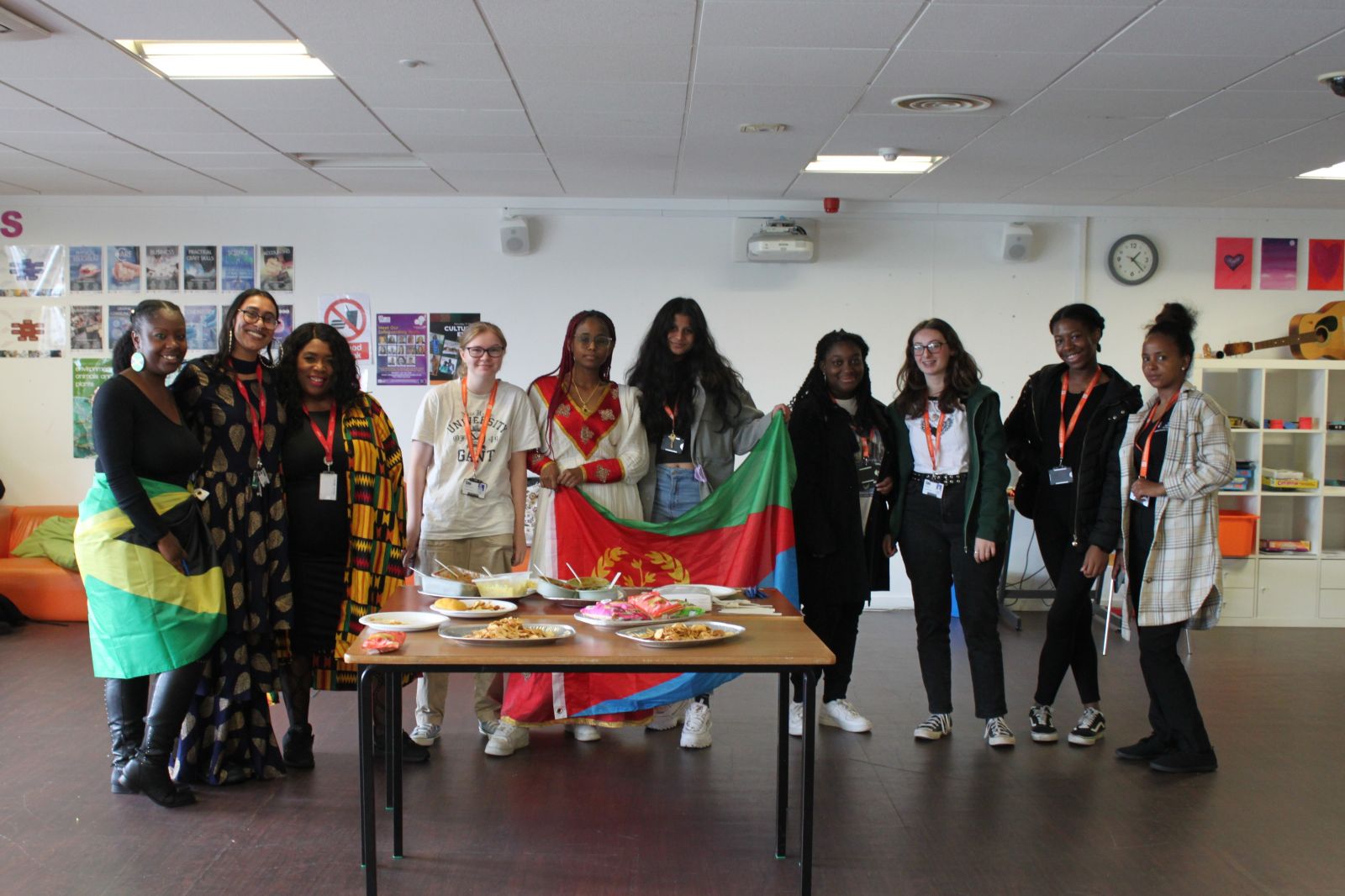 Students and staff holding flags, wearing traditional clothes behind a table of food